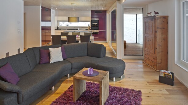 A modern living room with a grey sectional sofa, a small wooden coffee table, and a purple rug.