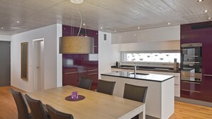 Cozinha moderna com ilha central, eletrodomésticos embutidos e área de refeições com mesa e cadeiras de madeira.