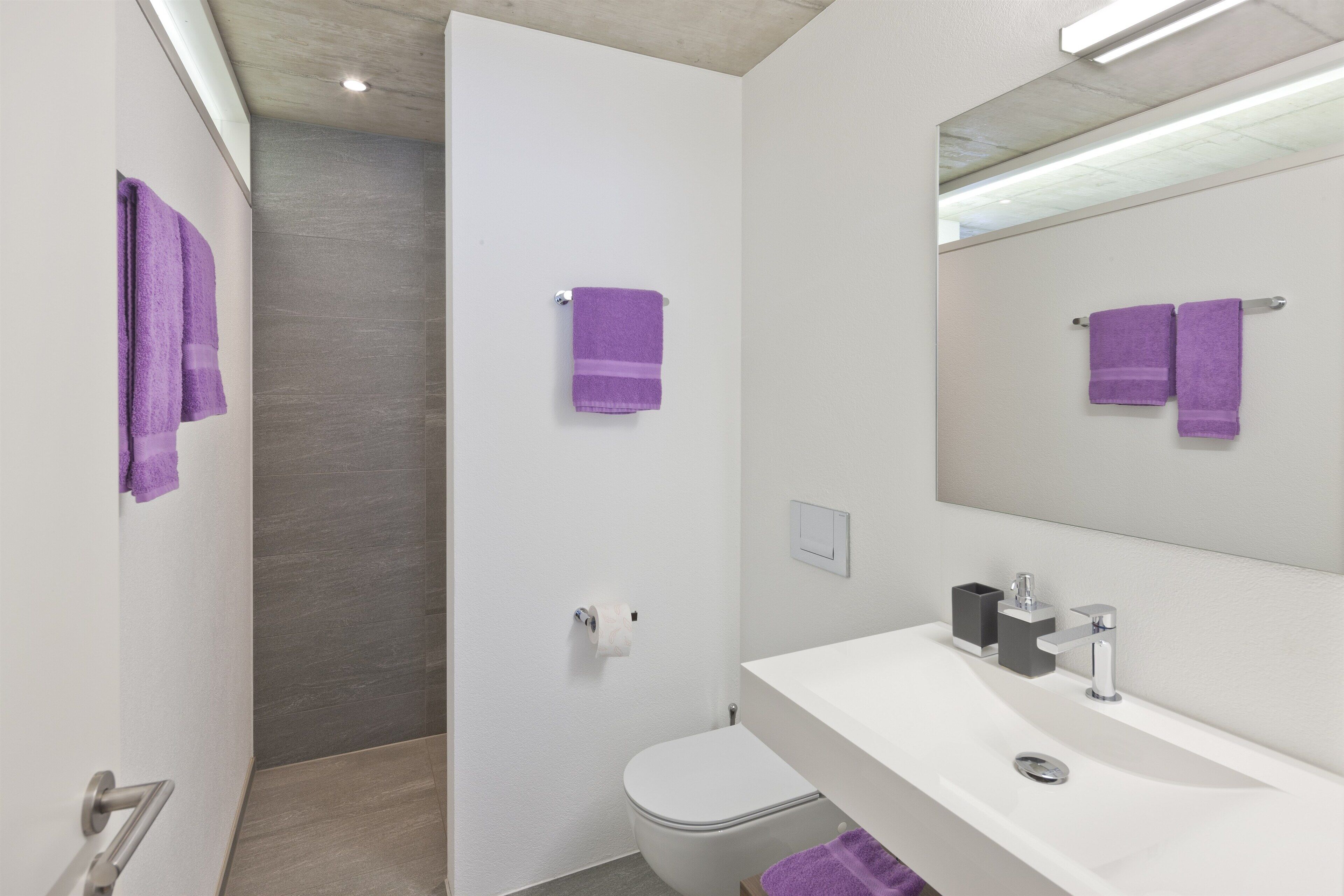 A modern bathroom with a white sink, a mirror, and two purple towels.