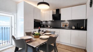 A modern kitchen with white cabinets, a dining table set for four, and a large window overlooking a balcony.