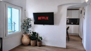 A modern living room with a large TV displaying 'NETFLIX', a potted plant, and a view of a balcony.