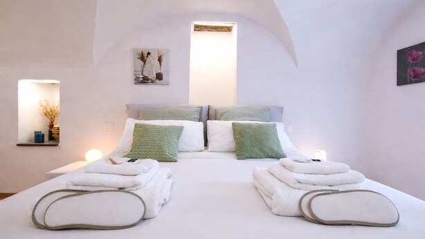 A bedroom with a large bed, two pillows, a bedside table with a lamp, and a wall-mounted artwork.