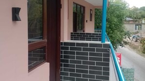 A building with a pink exterior, a balcony with blue railings, and a black tiled wall. - Hotel Nirmal (Palampur)