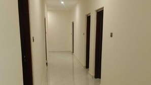 A hallway with white walls and a shiny floor, leading to several dark doors. - Hotel Nirmal (Palampur)