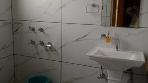 A bathroom with a white sink, a mirror, and a shower with a handheld showerhead. - Hotel Nirmal (Palampur)