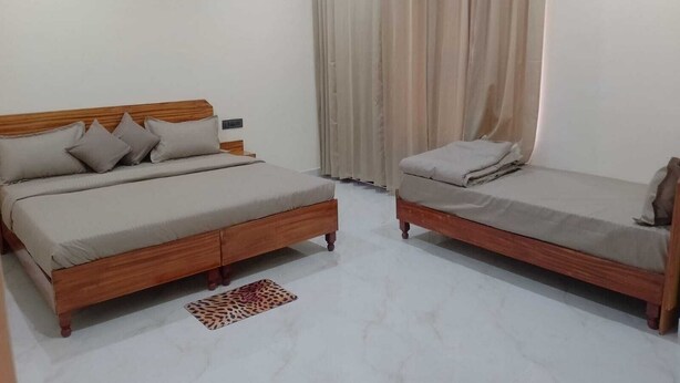 A bedroom with two beds, a wooden headboard, a nightstand, a patterned rug, and a window with curtains. - Hotel Nirmal (Palampur)