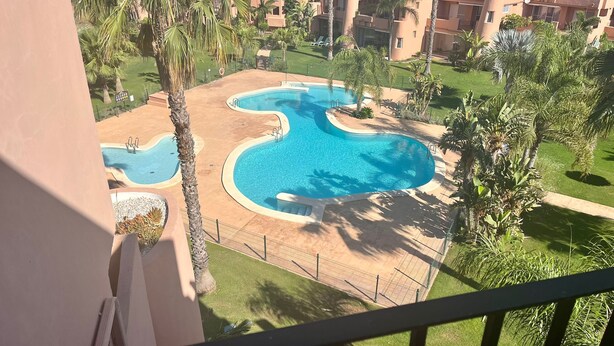 A pool area with multiple swimming pools, surrounded by palm trees and a fence. - **Introductory Discount** Gorgeous Apartment with Golf & Pool Views 14132 (Torre-Pacheco)