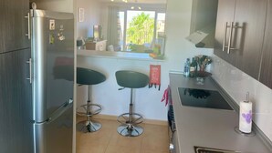 A modern kitchen with a refrigerator, two bar stools, a sink, and a window with a view of greenery. - **Introductory Discount** Gorgeous Apartment with Golf & Pool Views 14132 (Torre-Pacheco)
