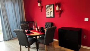 Ein Essbereich mit roter Wand, einem schwarzen Schrank und einem für vier Personen gedecktem Tisch mit schwarzen Stühlen.