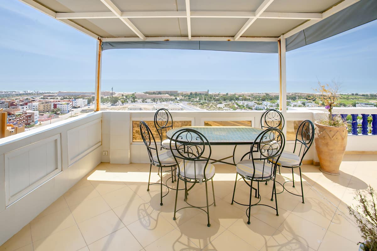 Un espacio al aire libre techado con mesa y sillas, con vista a un paisaje urbano.