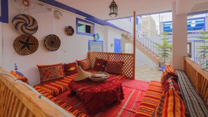 A room with a wooden bed, a red patterned sofa, and a woven basket on the floor. - BLUERINA CAMP HOSTEL (Aourir)