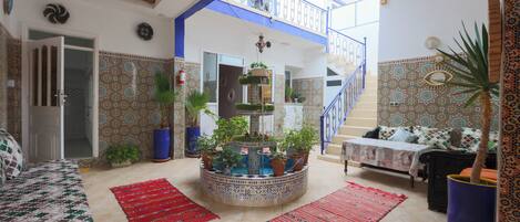A spacious living area with a high ceiling, a central fountain, and a staircase leading to an upper level.