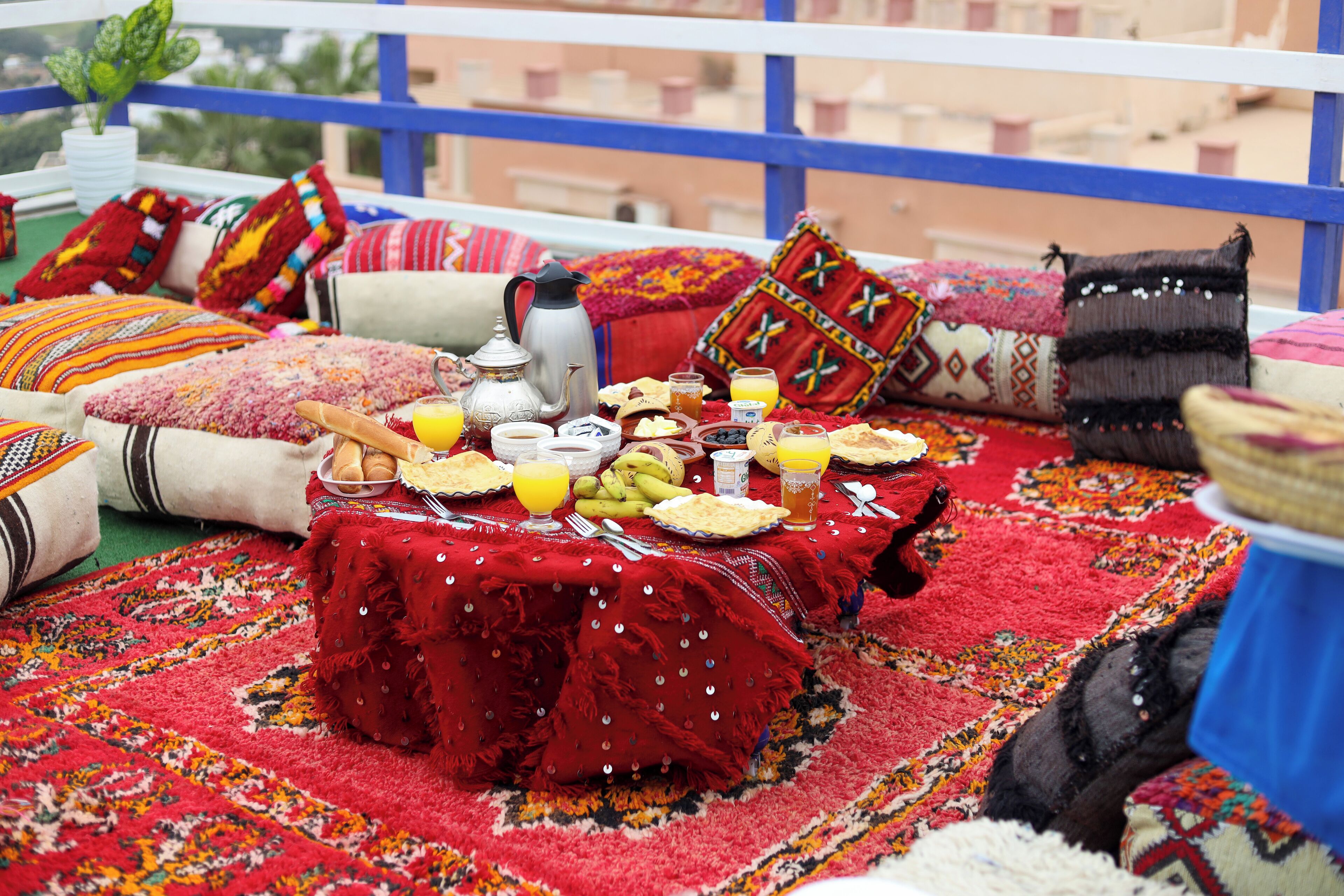A dining area with a table set for breakfast, surrounded by colorful pillows and a red rug.