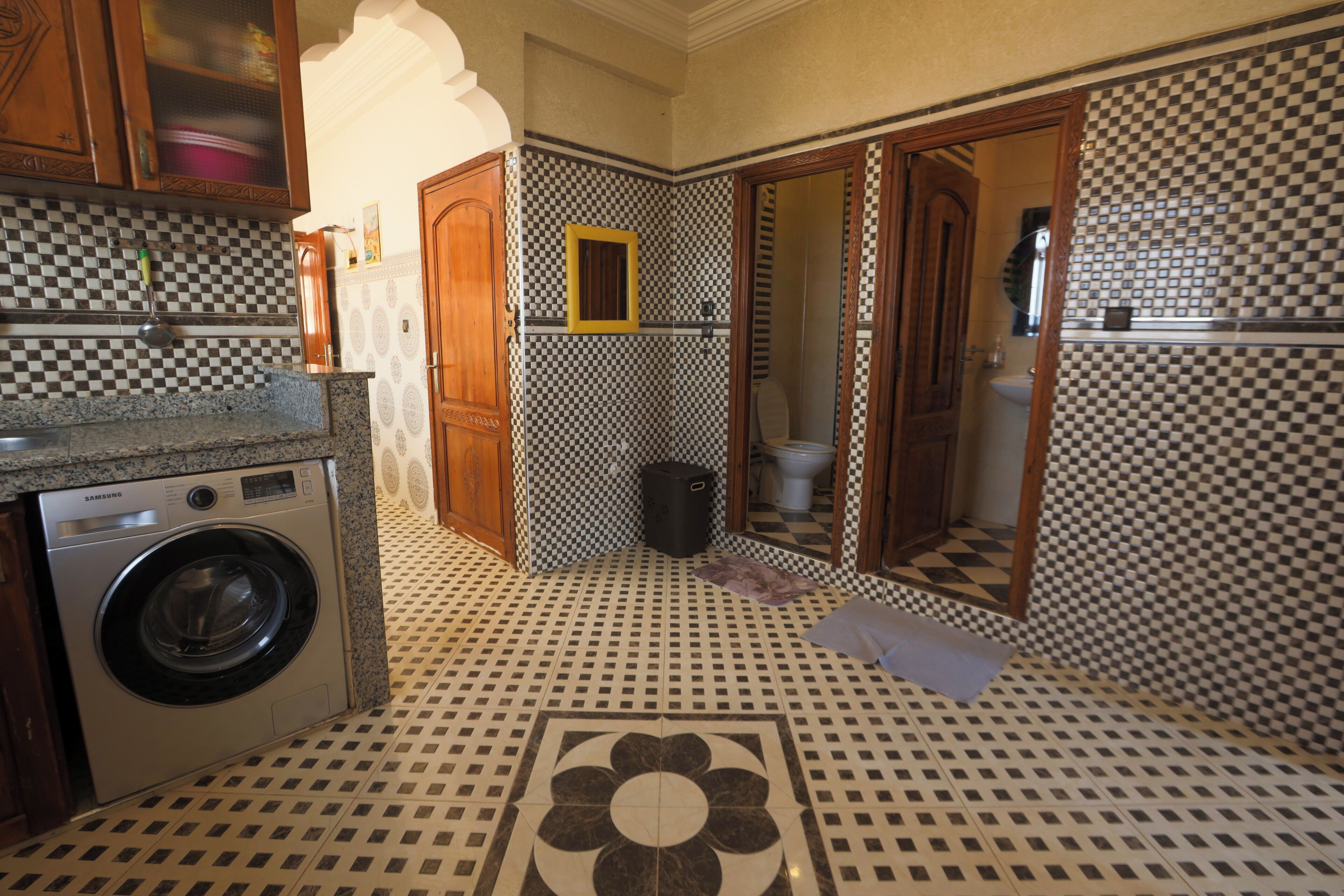 A compact kitchen with a washing machine, a sink, and a tiled floor with a geometric pattern.