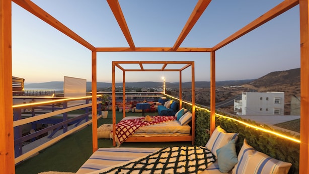 A rooftop terrace with a bed, seating area, and a view of the cityscape. - BLUERINA CAMP HOSTEL (Aourir)