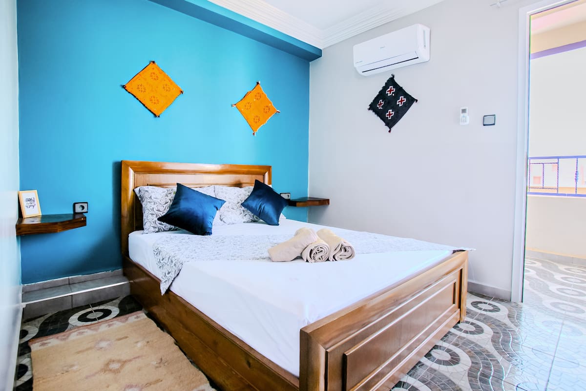 Un dormitorio con cama de madera, paredes azules y baldosas de suelo estampadas.
