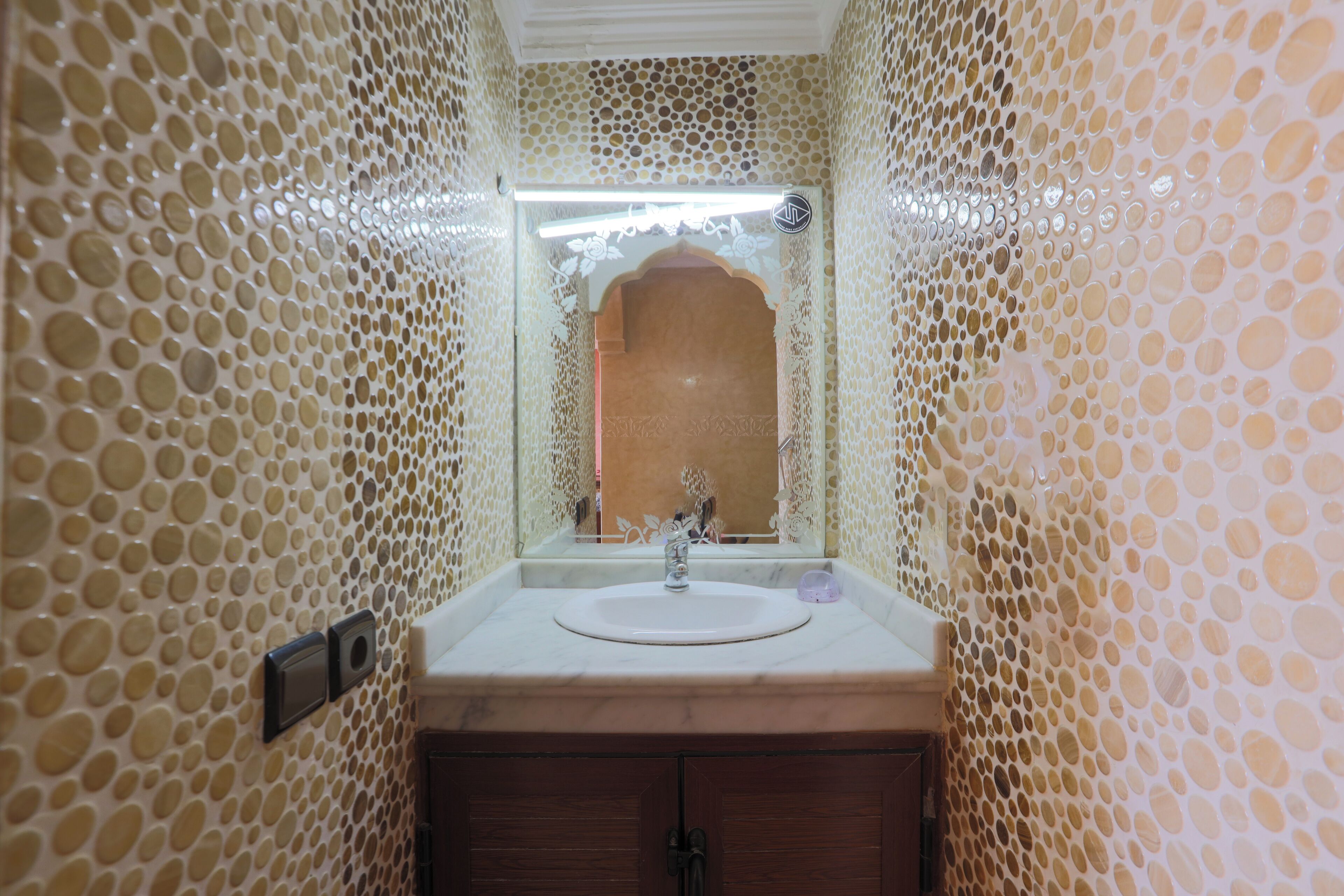 A bathroom with a circular mosaic wall design, a sink with a mirror, and a wooden cabinet.