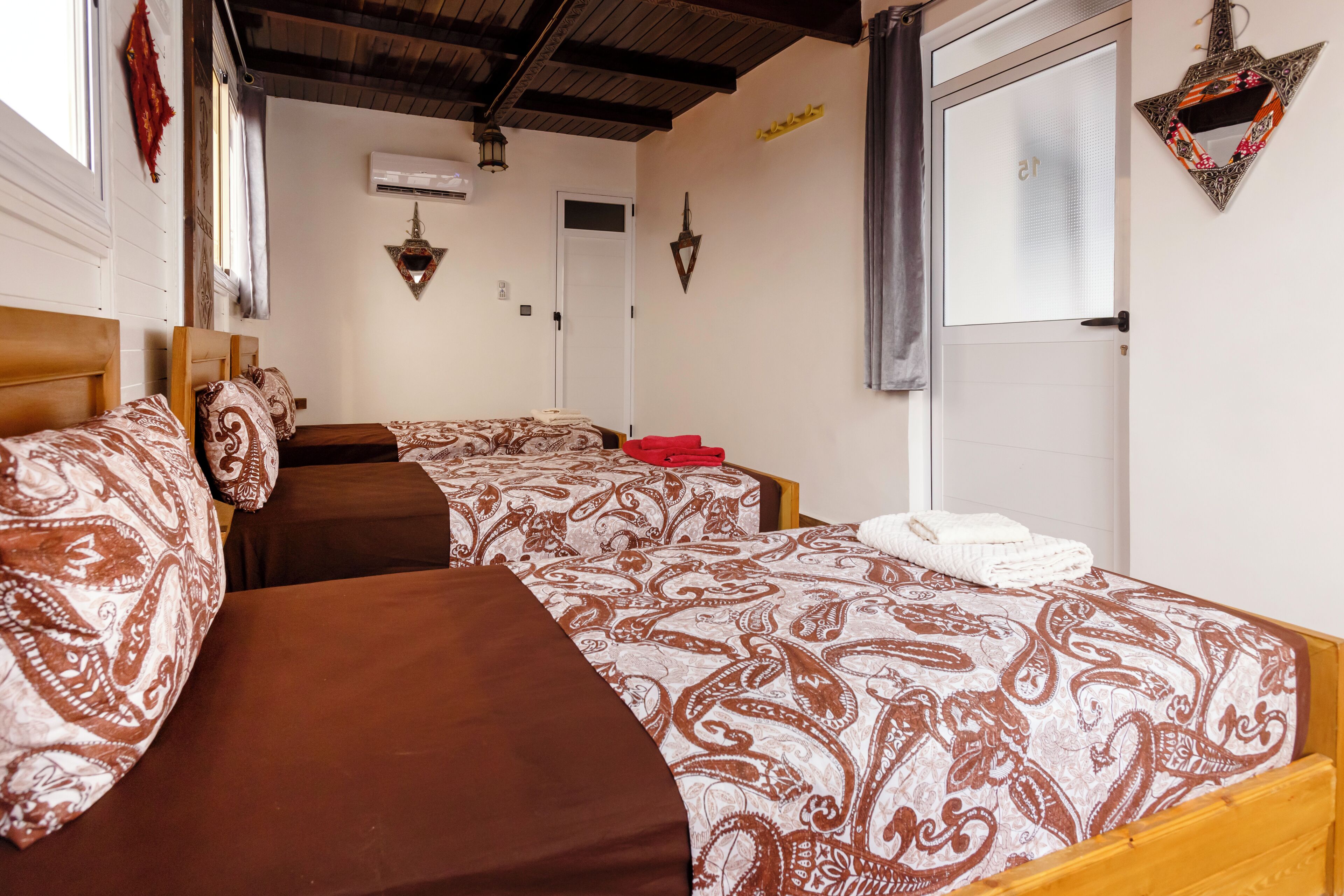 Habitación de hotel con dos camas, una ventana, un equipo de aire acondicionado y una puerta.
