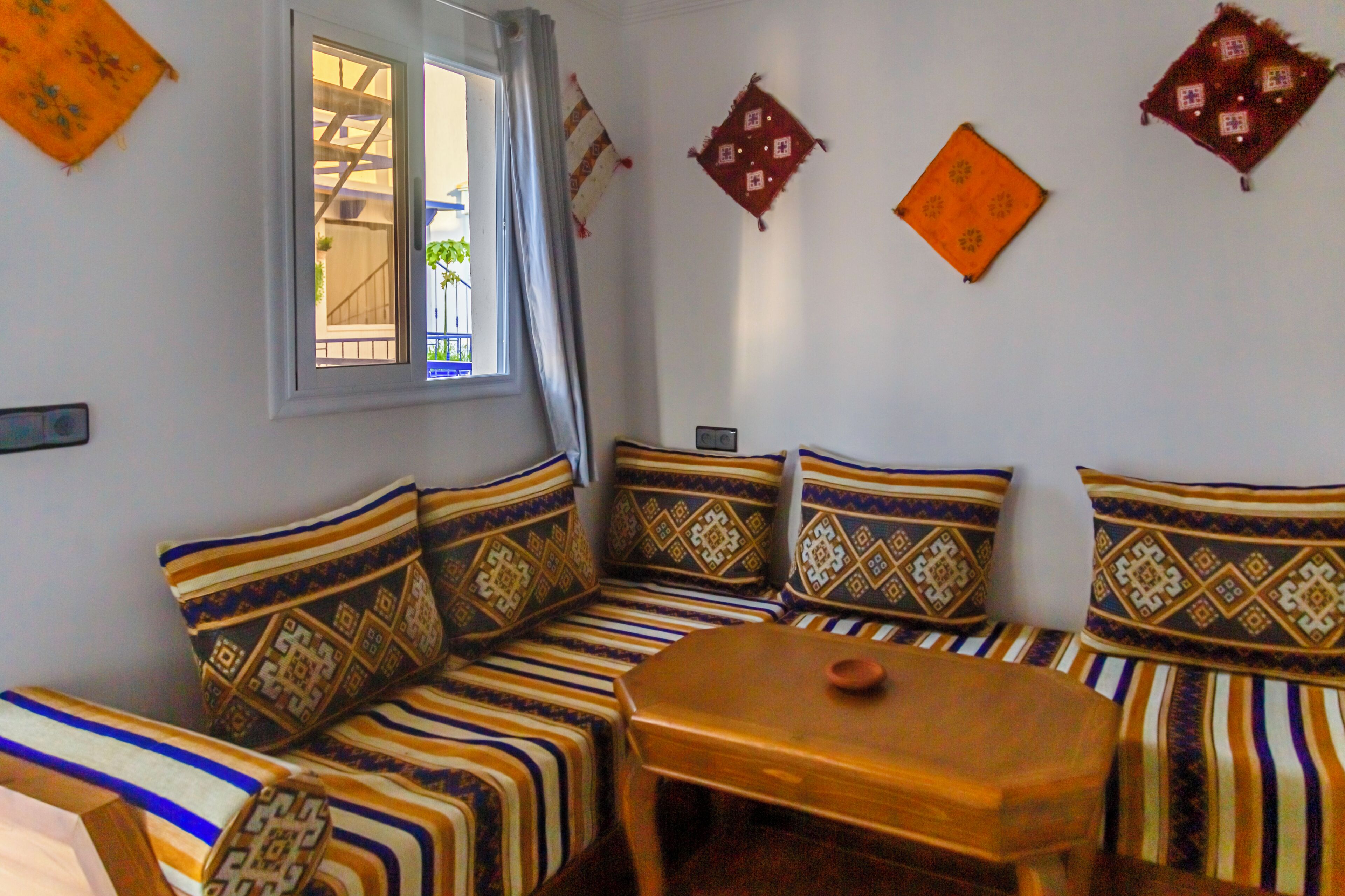 A room with a sofa set, a small wooden table, and patterned cushions.