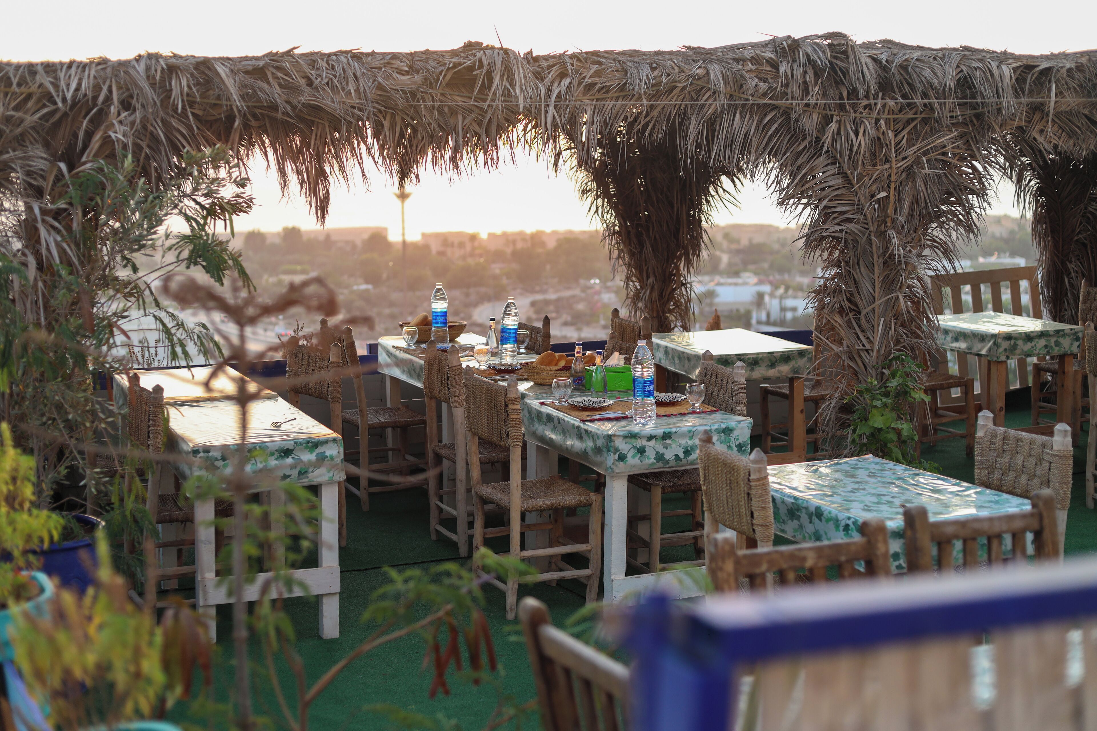An outdoor dining area with tables and chairs, some with umbrellas, and a view of the cityscape in the background.