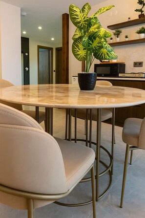 A modern dining area with a round table, two beige chairs, and a potted plant with variegated leaves.