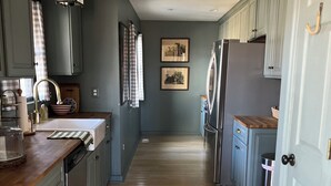 A kitchen with light blue cabinets, a wooden countertop, a stainless steel refrigerator, and a hanging light fixture.