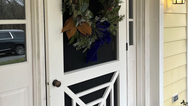 A white front door with a decorative wreath, a geometric window design, and a stone step leading to the entrance.