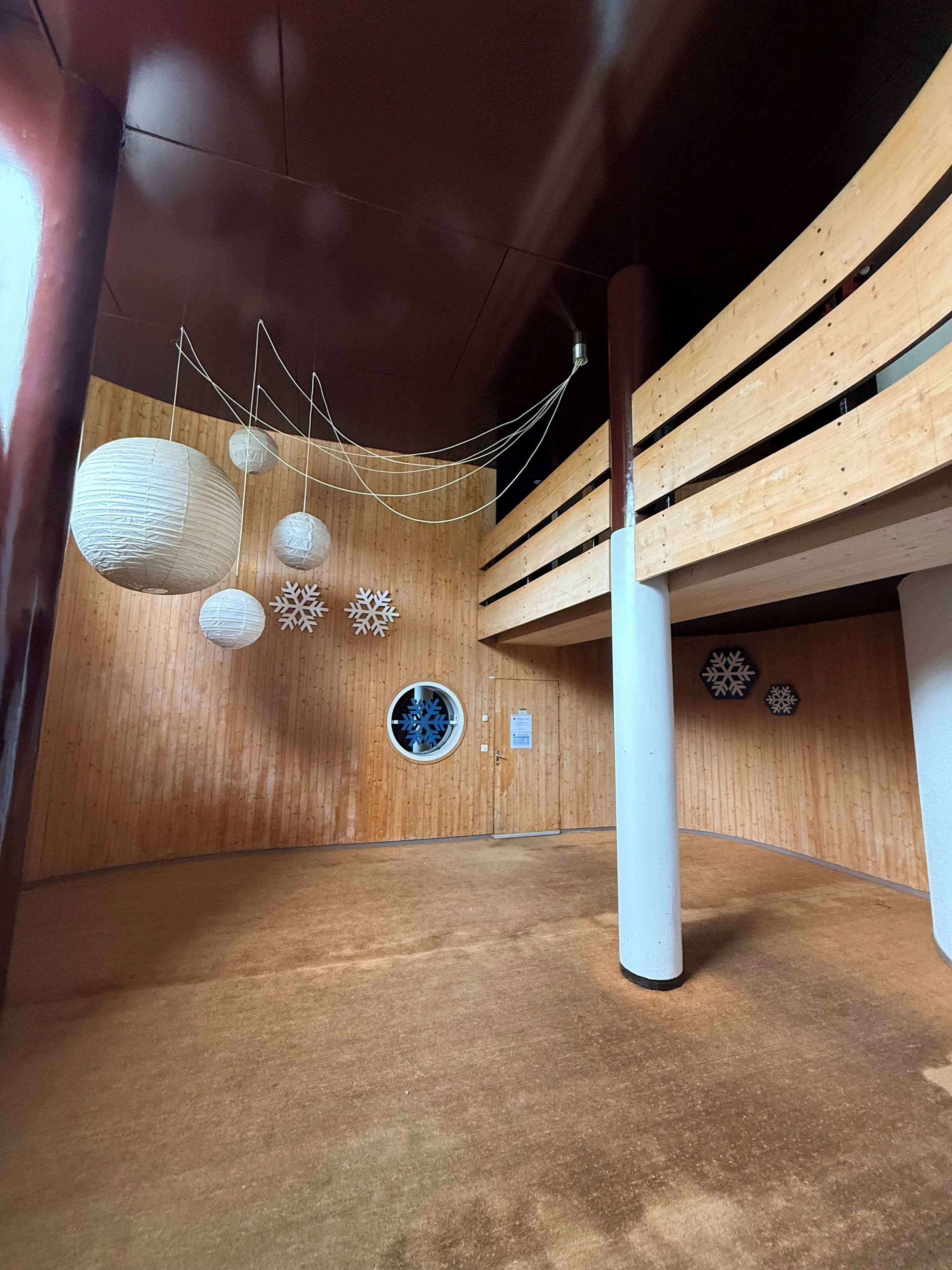 Um espaço amplo e interno, com paredes de painéis de madeira, teto alto e lanternas de papel penduradas.