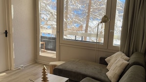 A cozy living room with a sofa, a small table, and a window with a view of snow-covered trees. - ⛷ T2 Cabin - At the foot of the slopes, Exceptional view (Vars)