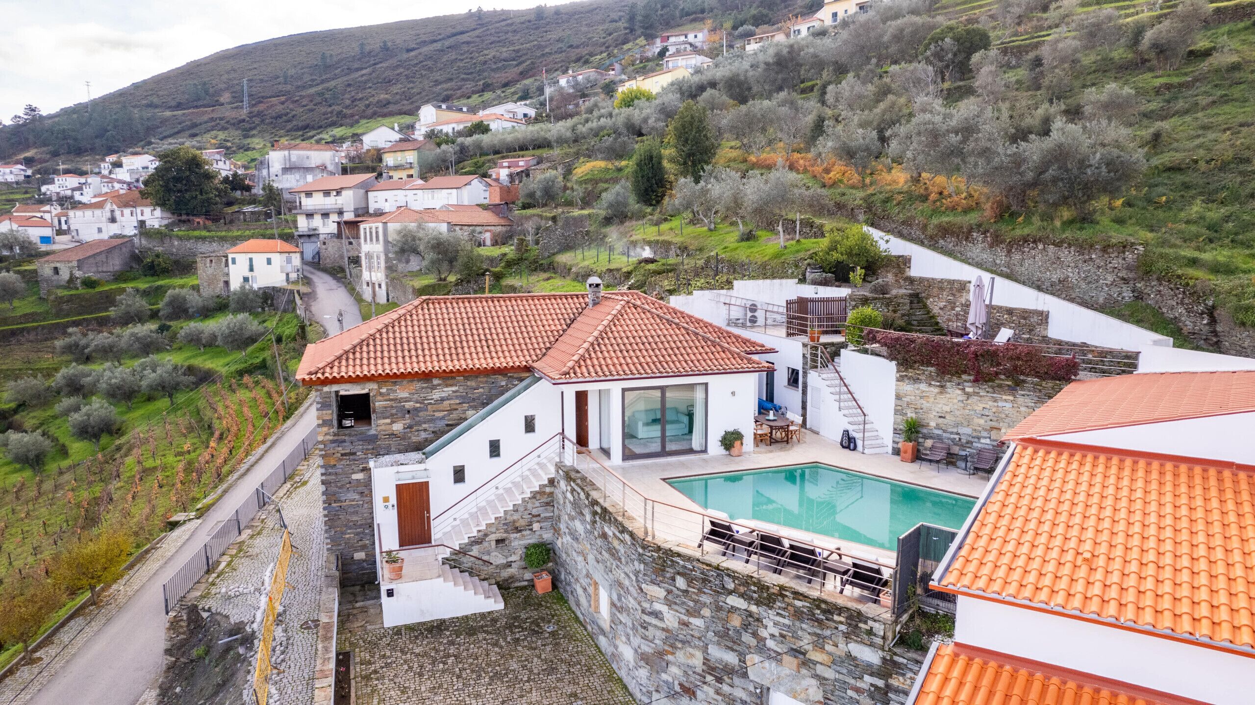 Une propriété située sur une colline, dotée d’une piscine, de murs en pierre et offrant une vue sur le village environnant.