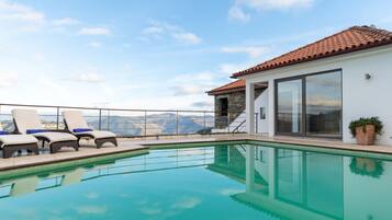 Zona junto a la piscina con sillones de descanso y vistas a las montañas.