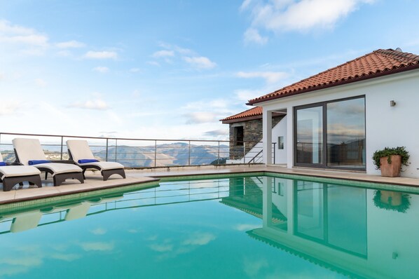 A poolside area with lounge chairs and a view of mountains.