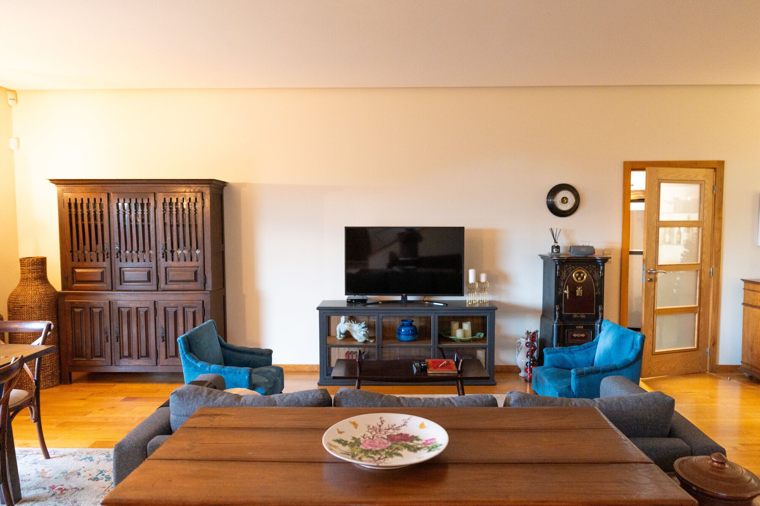 Una sala de estar con un aparador de madera, un televisor y dos sillones azules.