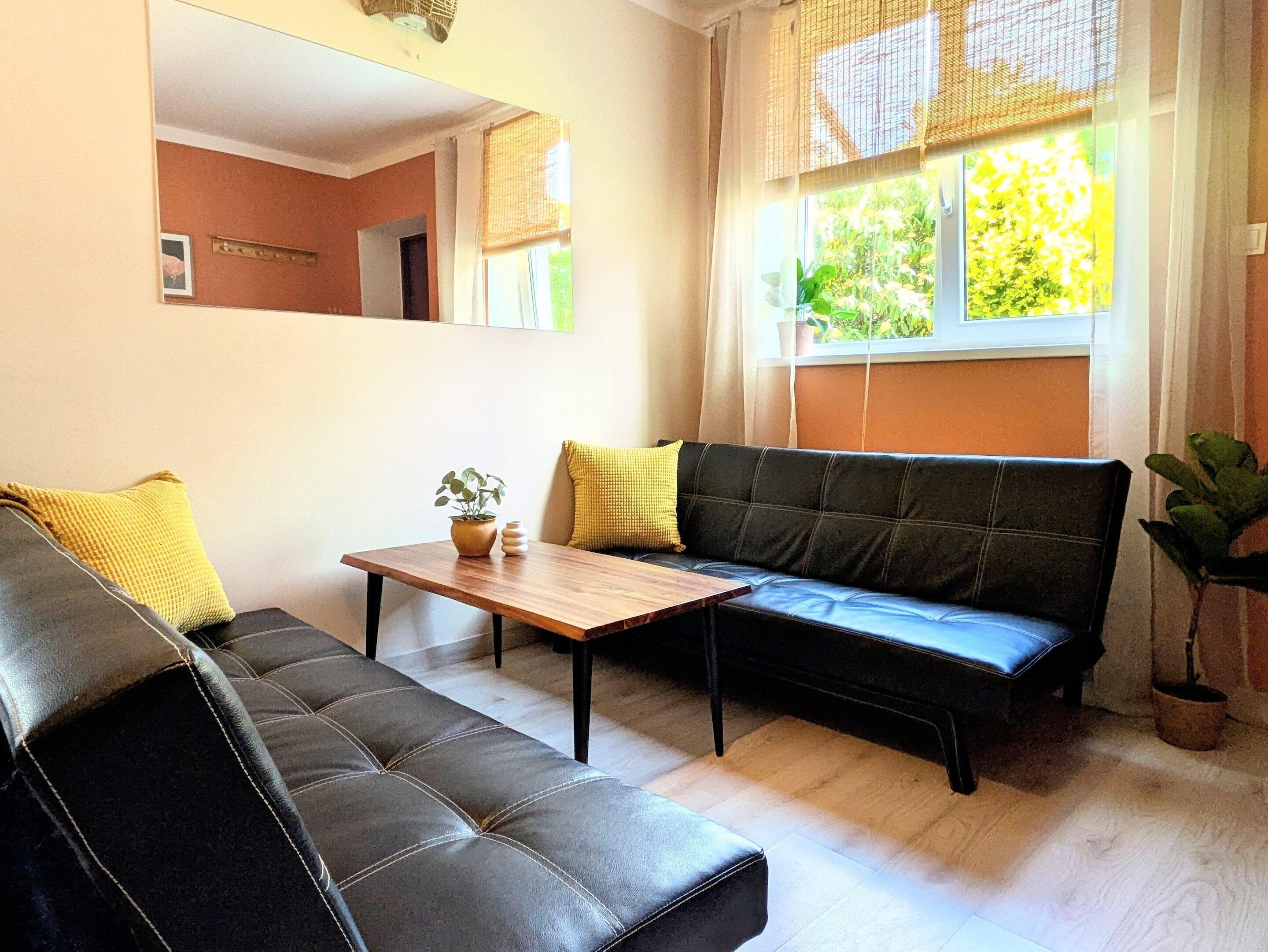A living room with a sofa, a coffee table, and a window with a view of greenery.