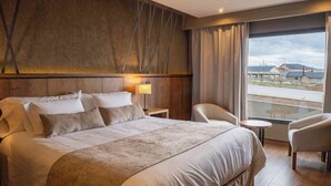 A hotel room with a large bed, a chair, a small table, and a view of the outside. - Hotel Ayres de Calafate (El Calafate)