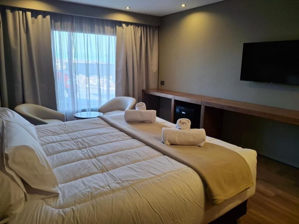 A hotel room with a large bed, two chairs, a small table, a flat-screen TV, and a window with curtains.