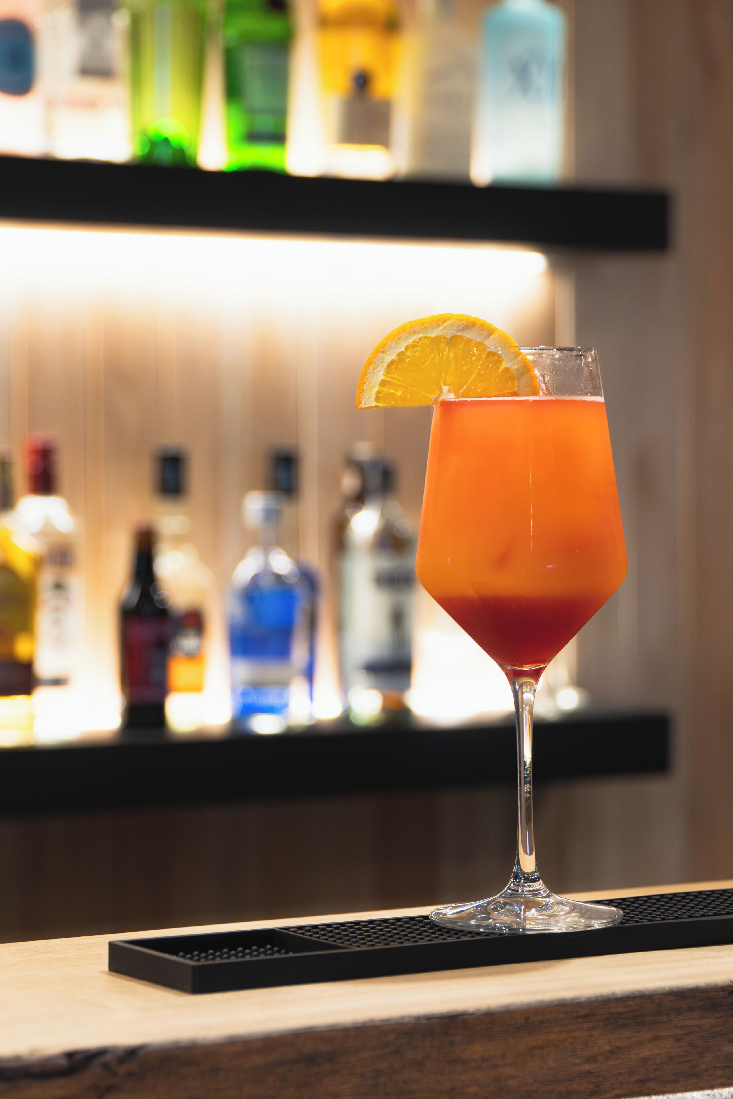 A cocktail glass with an orange slice garnish on a bar counter.