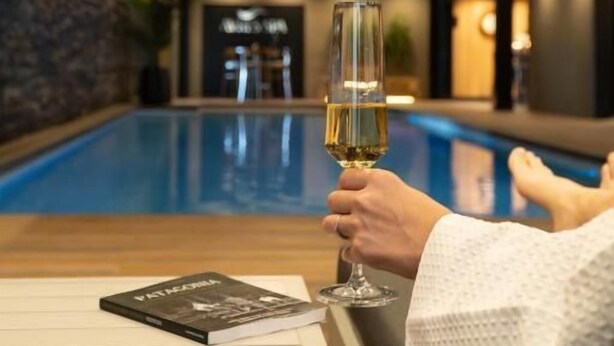 A person relaxing by a pool with a glass of wine, a book on the table, and a sign in the background. - Hotel Ayres de Calafate (El Calafate)