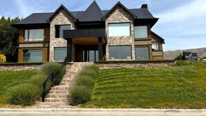 A modern two-story house with a stone facade, large windows, and a prominent front entrance. - Hotel Ayres de Calafate (El Calafate)