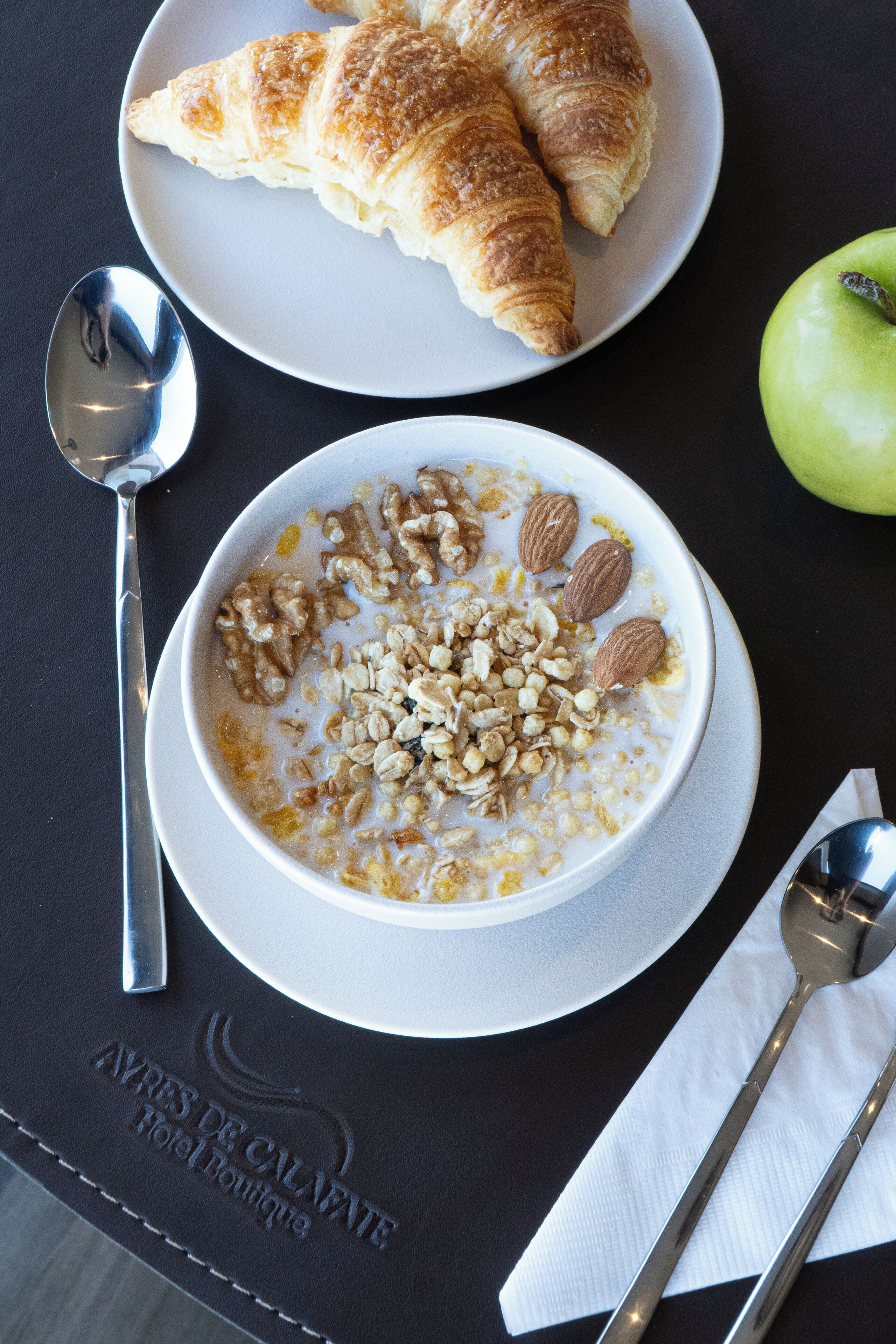 Una mesa con un tazón de avena, un croissant y una manzana.