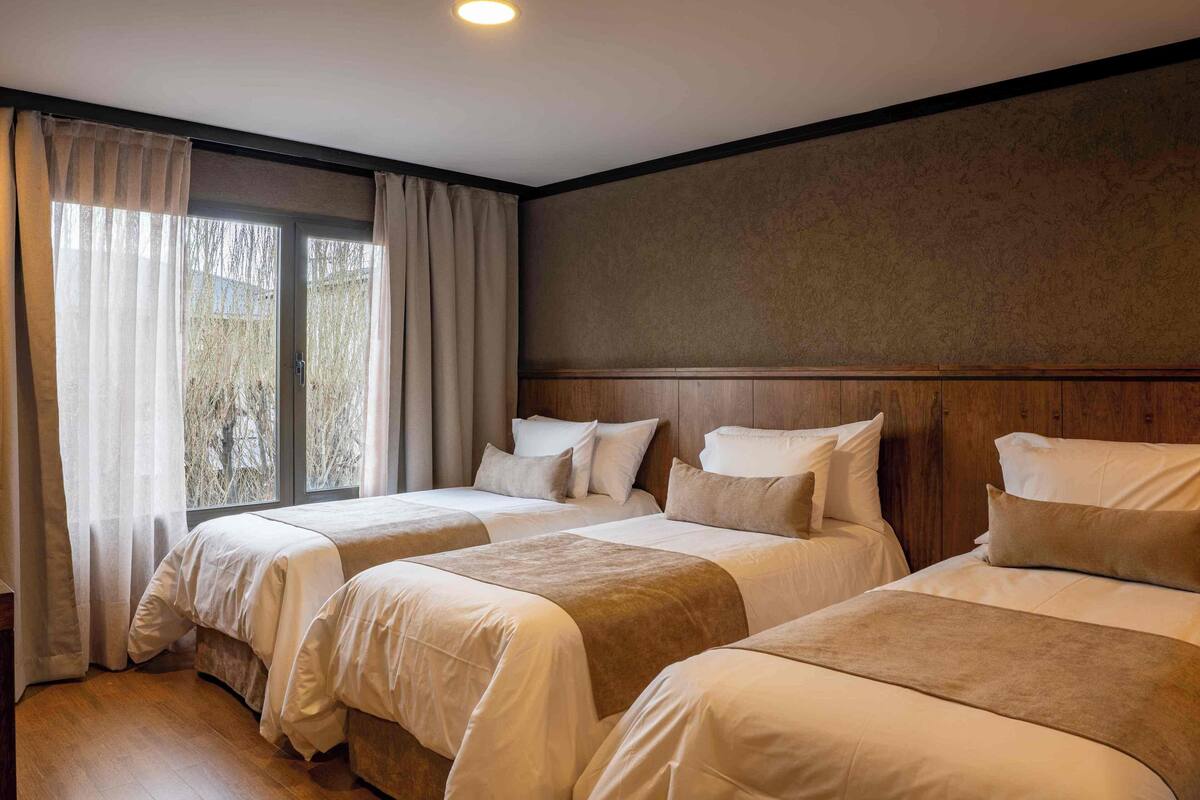 A hotel room with three beds, a large window with curtains, and a wooden headboard.