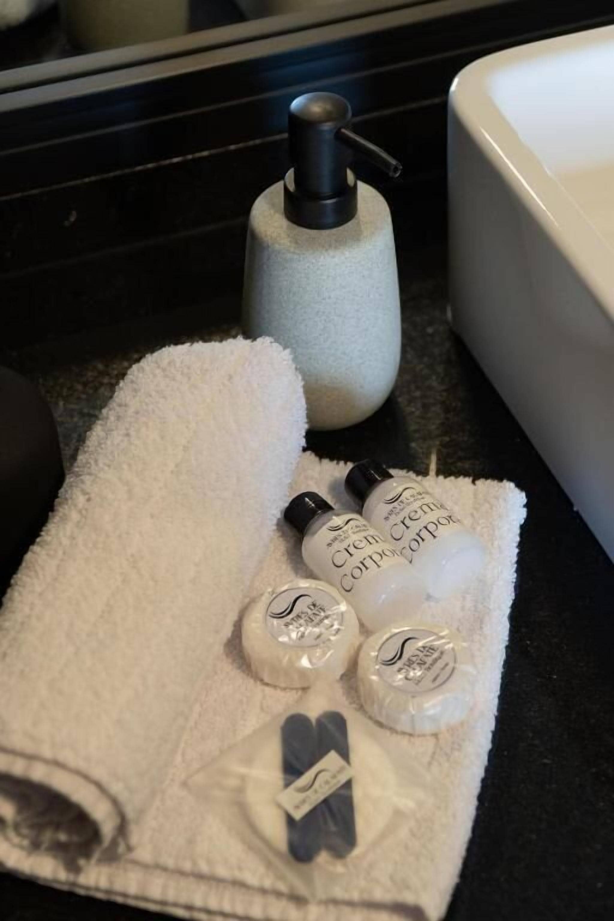 Een badkamer met een witte handdoek, een zeepdispenser en diverse toiletartikelen op een aanrecht.
