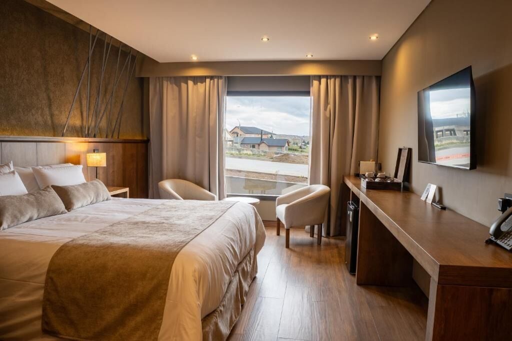 Une chambre d’hôtel avec un grand lit, un bureau, une chaise et un téléviseur fixé au mur.