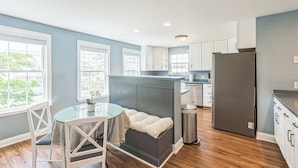 A modern kitchen with white cabinets, a grey refrigerator, and a dining area with a glass table and white chairs.