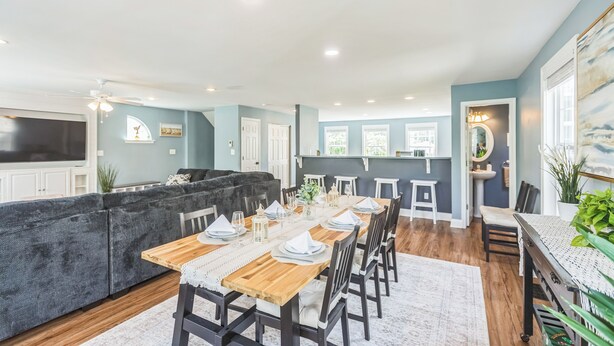 A dining area with a wooden table set for six, surrounded by dark chairs.