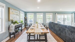 A dining room with a wooden table set for six, flanked by chairs, a grey sofa, and a console table with plants.