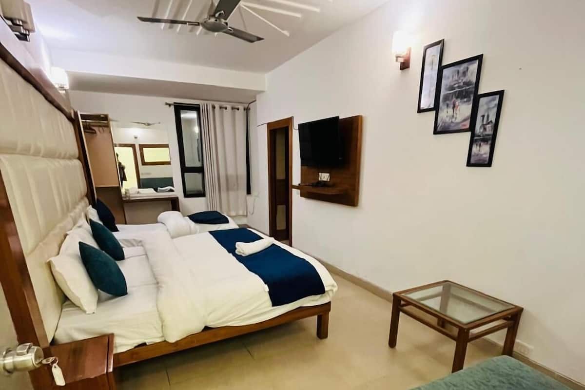 Une chambre d’hôtel avec un lit, un canapé vert, une petite table, un ventilateur de plafond et un téléviseur fixé au mur.