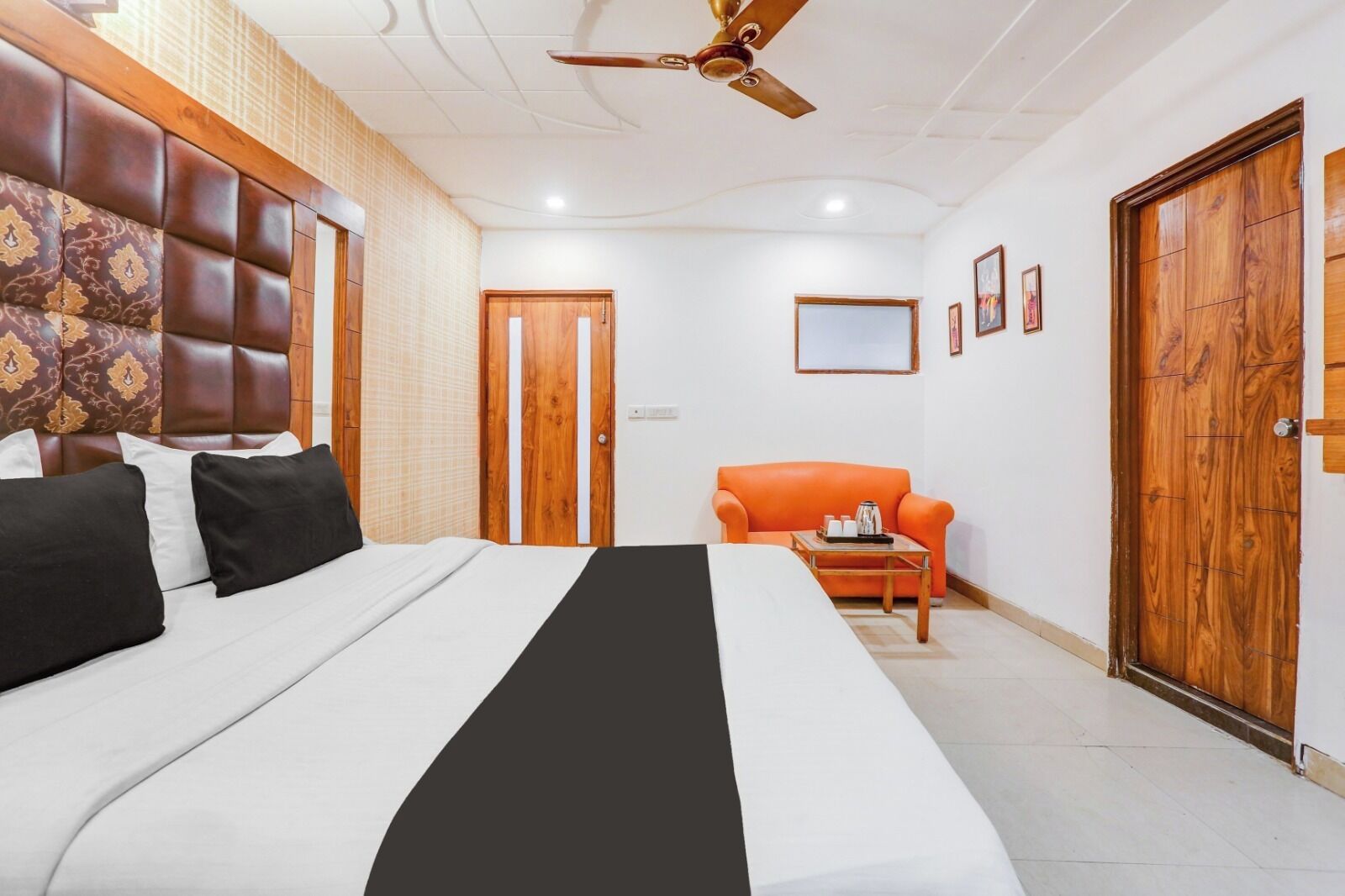 Ein Hotelzimmer mit einem großen Bett, einem Deckenventilator, einem orangefarbenen Sessel und Holztüren.
