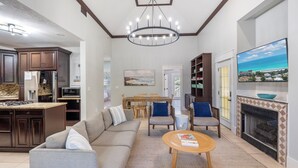 Una sala moderna con sofá, mesa de centro y chimenea. Cuenta con un comedor con mesa y sillas, y una cocina con armarios de madera oscura y encimera de granito.