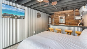Una habitación de hotel moderna con una cama grande, kitchenette y vistas a un paisaje urbano.